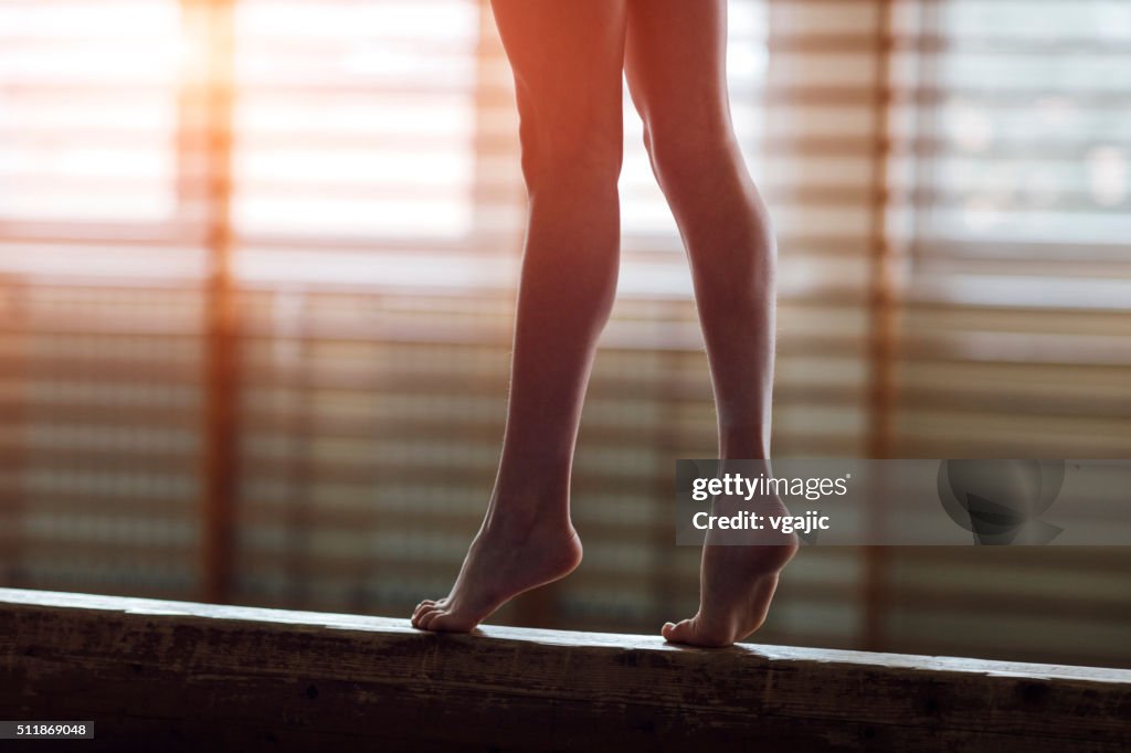 Female gymnast walking on balance beam, low section