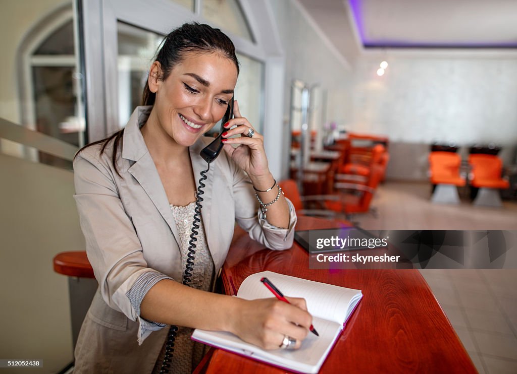 Smiling receptionist making appointment over the phone.