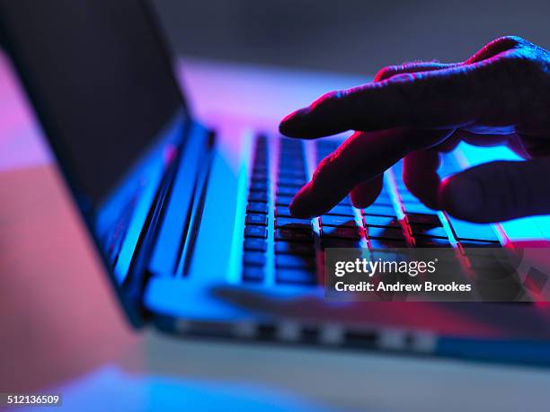 silhouette of male hand typing on laptop keyboard at night - dark background light stock-fotos und bilder