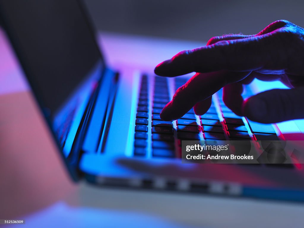 Silhouette of male hand typing on laptop keyboard at night