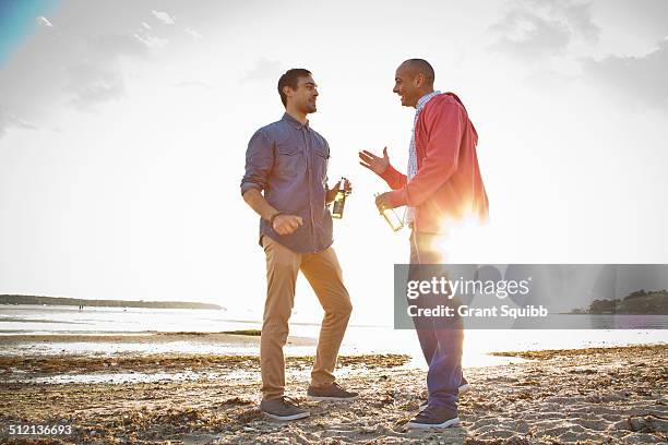 men drinking beer and chatting on beach - man sipping beer smiling stockfoto's en -beelden