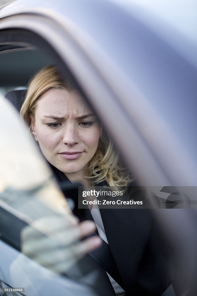 Worried businesswoman reading texts on smartphone in city traffic jam