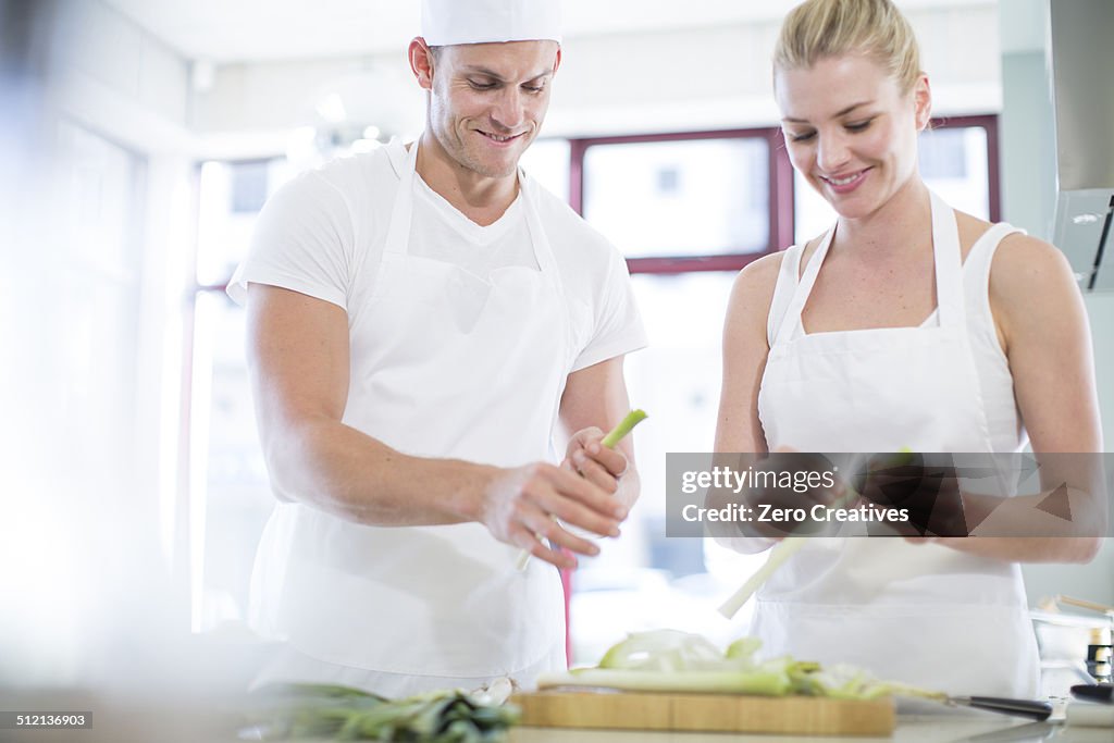 Male and female chefs peeling leeks in commercial kitchen