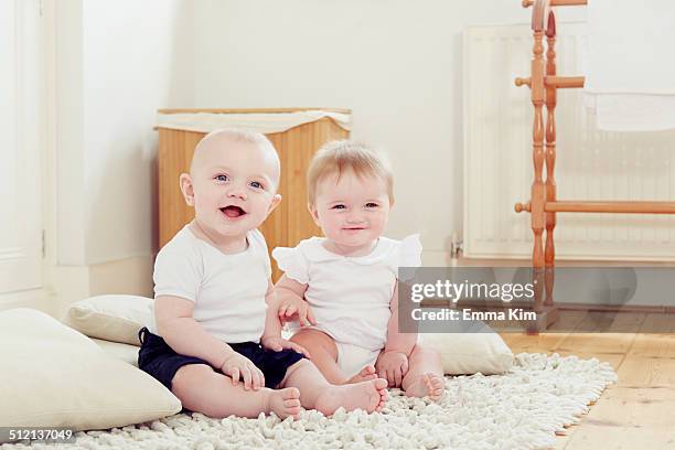 portrait of smiling baby girl and baby boy sitting on rug - baby girl stock pictures, royalty-free photos & images