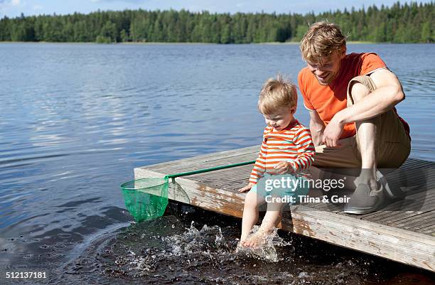 father and son sitting on lake pier, somerniemi, finland - finland happy stock pictures, royalty-free photos & images