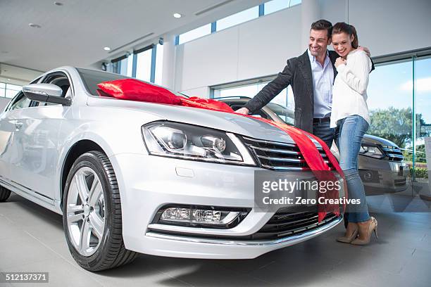 man looking at new car with red bow with girlfriend in car dealership - auto nuevo fotografías e imágenes de stock