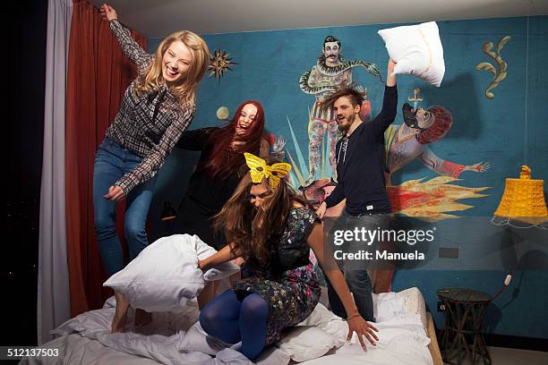 four adult friends having pillow fight on hotel bed - pillow fight stock pictures, royalty-free photos & images