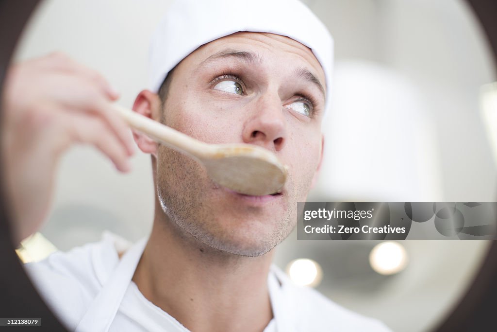 Male chef tasting food from saucepan in commercial kitchen