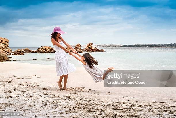 young woman swinging daughter on beach, la maddalena, sardinia, italy - sardegna foto e immagini stock