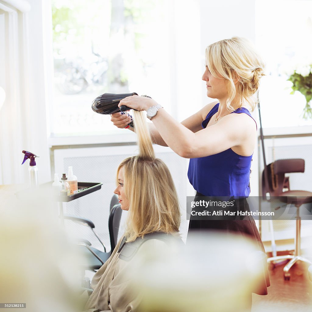 Hairdresser drying customer's hair with hairdryer