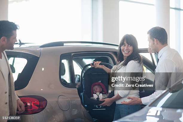 mid adult couple with baby girl trying out baby seat in car dealership - baby carrier stock pictures, royalty-free photos & images