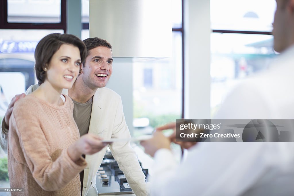 Mid adult couple and salesman looking at ceramic tile in kitchen showroom