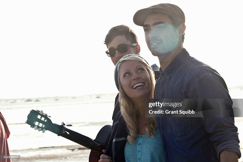 Three adult friends with acoustic guitar on Bournemouth beach, Dorset, UK