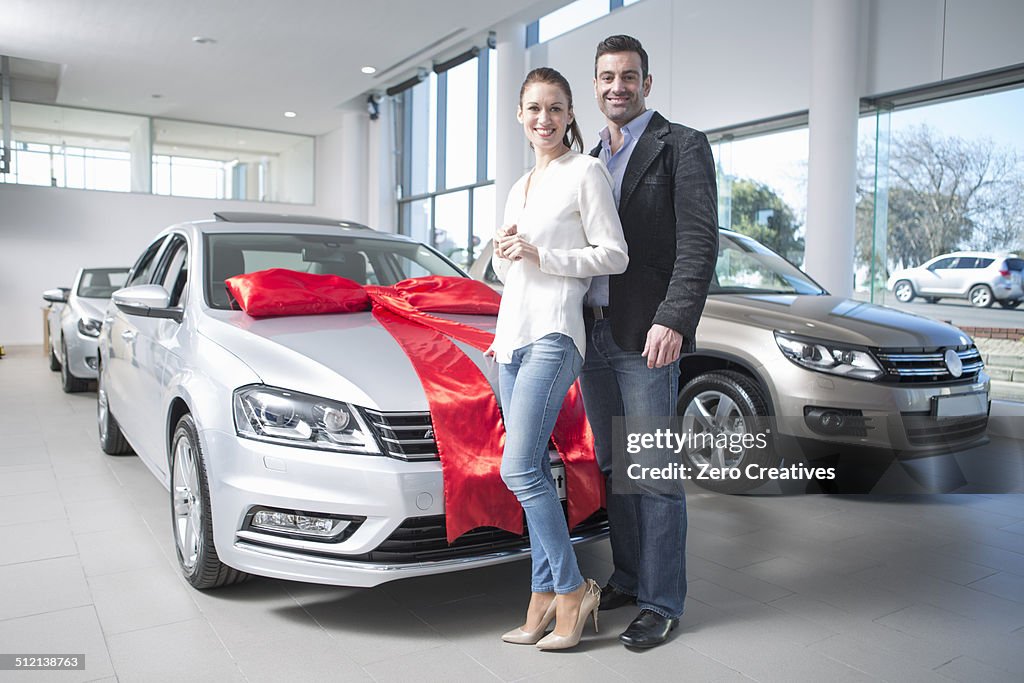 Portrait of mid adult couple and new car with red bow in car dealership