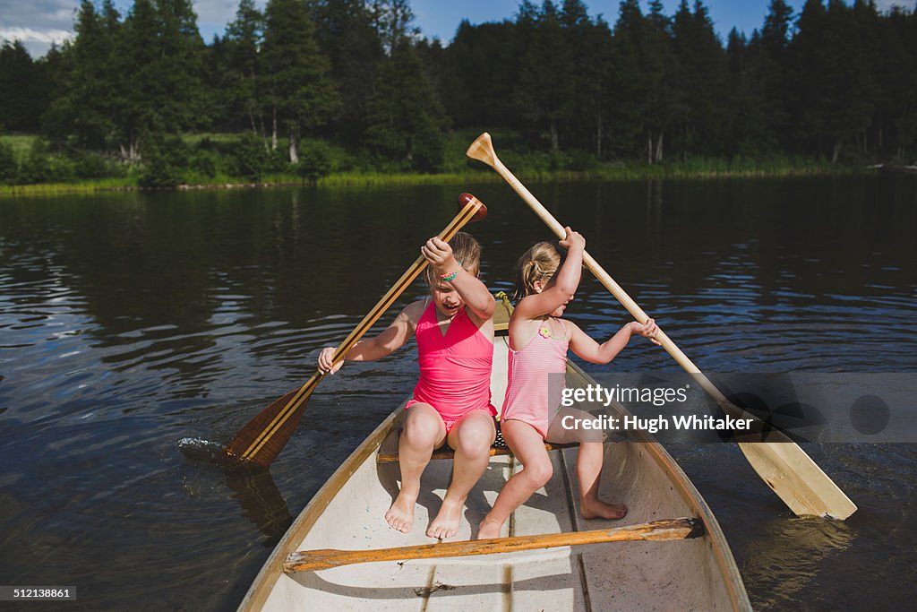 Two young sisters rowing in canoe on Indian river, Ontario, Canada