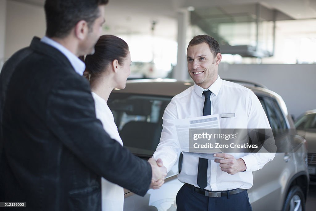 Mid adult couple making deal with salesman in car dealership