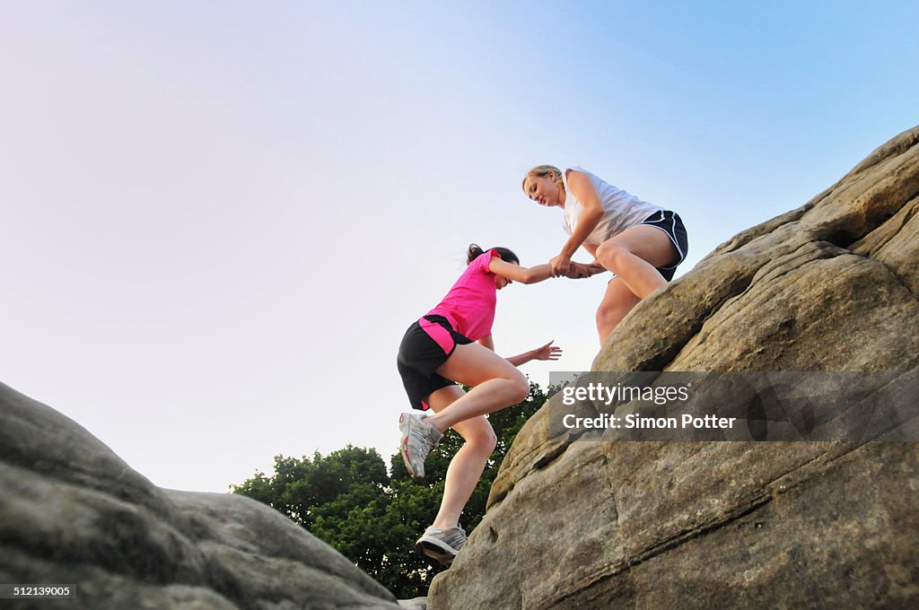 Two young women runners helping each other on top of rock formation