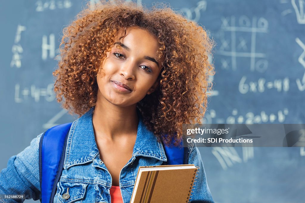 Teen student with curly hair standing in front of blackboard