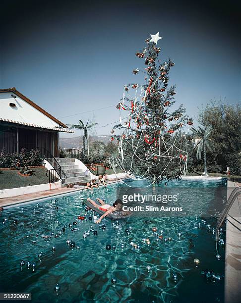 Premium Rates Apply. Rita Aarons, wife of photographer Slim Aarons, swimming in a pool festooned with floating baubles and a decorated Christmas...