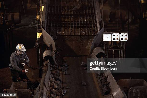 Worker moves a heavy chain while working beside a conveyor belt carrying coking coal in a processing facility above ground in the Piniowek coal mine,...