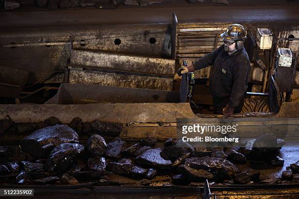 Worker watches as large lumps of coking coal move along a conveyor belt in a processing facility above ground in the Piniowek coal mine, operated by...