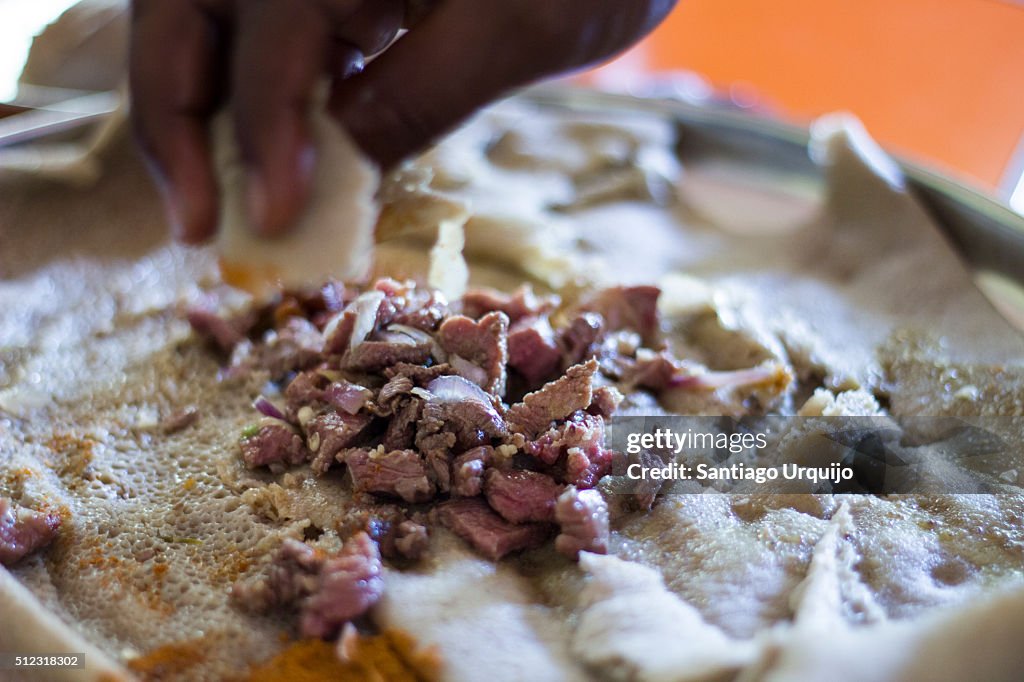 Hand picking up meat from a tray with injera