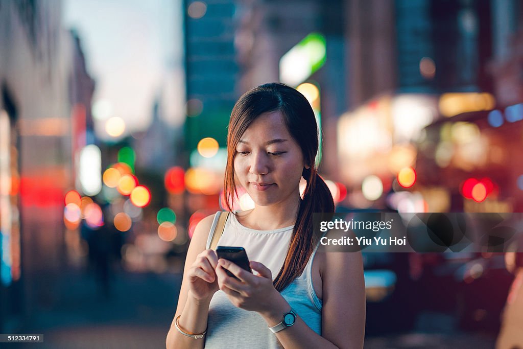 Young lady using smartphone in busy city street