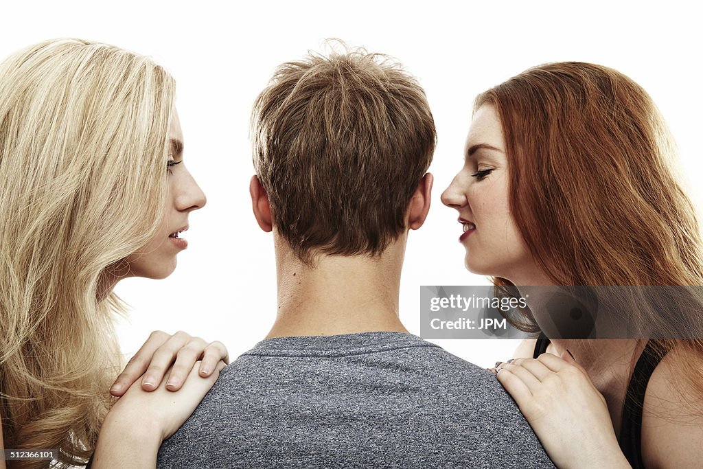 Studio portrait of two young woman whispering into young man's ears