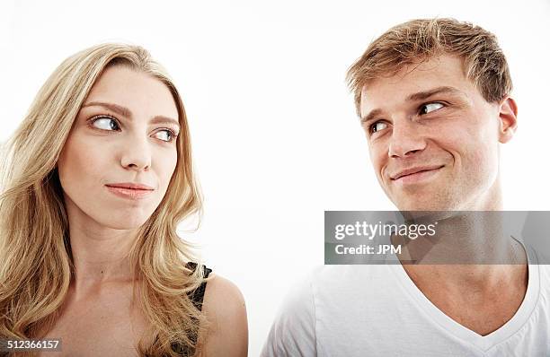 studio portrait of young couple looking sideways at each other - smirking stock pictures, royalty-free photos & images