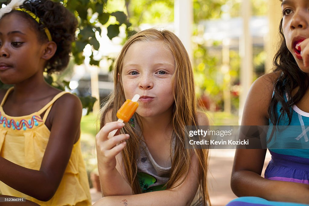 Portrait of three girls eating ice lollies in garden