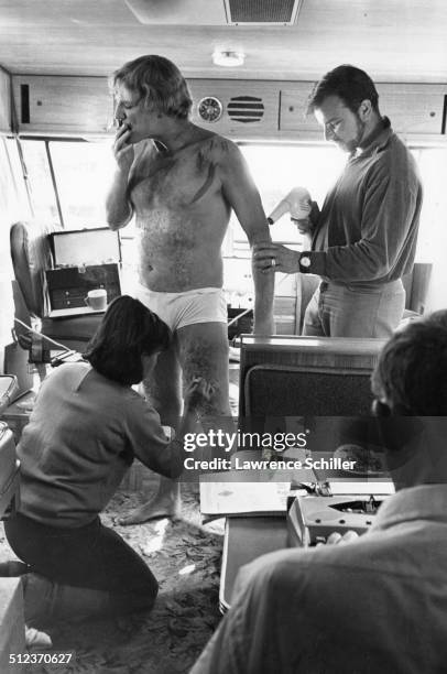In his trailer, Irish actor Richard Harris smokes a cigarette as make-up artists apply mud and 'injuries' to him, during production of the film 'A...