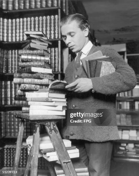 Young man peruses a stack of leather-bound novels in a library.