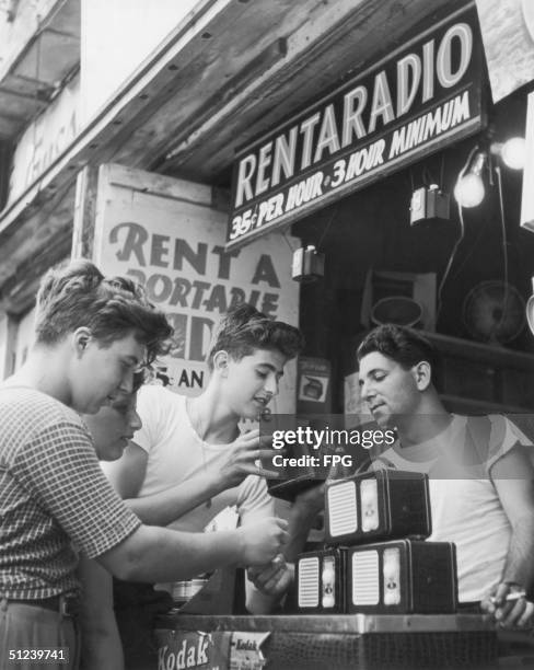 Circa 1950, Teenage boys hang out at a shop offering radios for rent at 35 cents per hour.