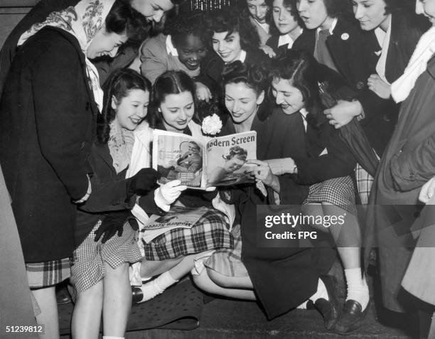 Circa 1950, Female fans of Frank Sinatra gaze adoringly at a picture of him in a copy of Modern Screen magazine, whilst awaiting his appearance at...