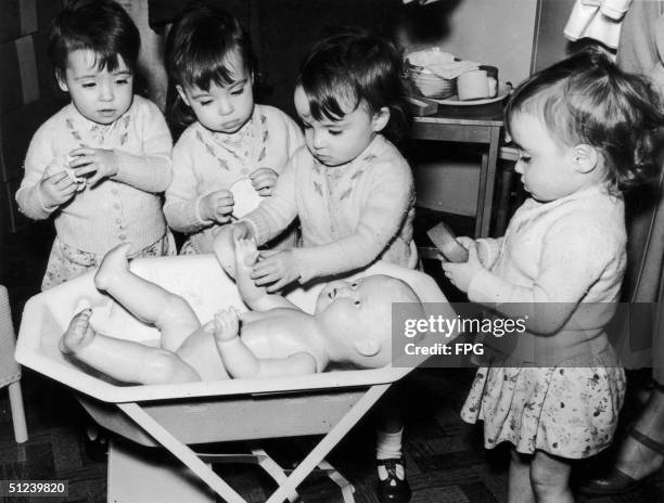 Circa 1940, The two-year-old Cole quadruplets learn to bathe a large doll at the Mothercraft exhibition in London's Central Hall.