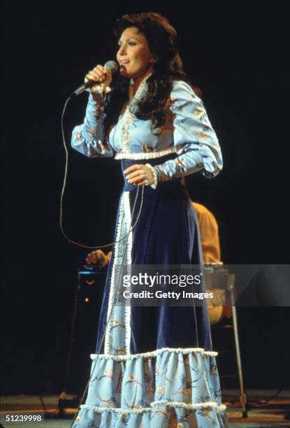 Circa 1980, American country singer and songwriter Loretta Lynn performs on stage, wearing a long dress.