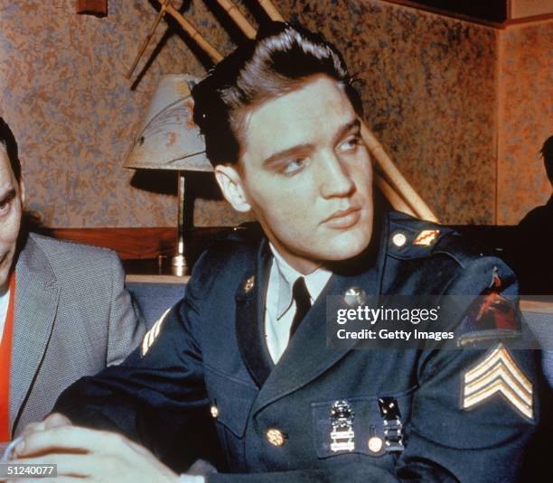 Circa 1958, American singer and actor Elvis Presley sits in a restaurant wearing his US Army uniform.