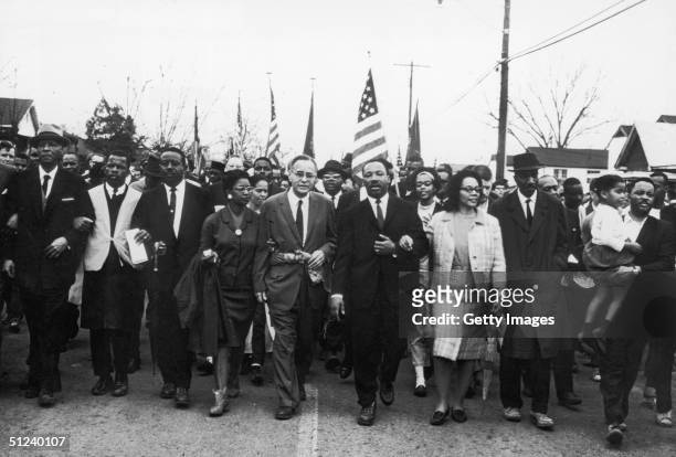 Circa 1965, American civil rights leader Dr Martin Luther King Jr and his wife Coretta Scott King lead a march down the center of a street, 1960s.