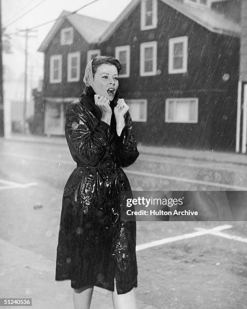 Circa 1940, A young woman turns up the collar of her raincoat against the downpour.