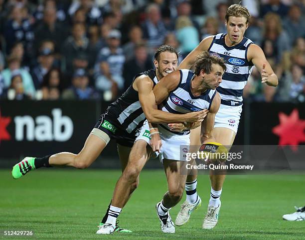 Corey Enright of the Cats handballs whilst being tackled by James Aish of the Magpies during the 2016 NAB Challenge match between the Geelong Cats...