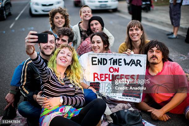 Protestors pose for a selfie while holding a placard reading 'End The war on Refugees' during a candlelight vigil as protestors stand in solidarity...