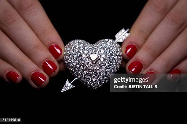 Gallery assistant poses for a photograph with a diamond brooch at Sotheby's auctioneers in London on February 26 to preview the forthcoming auction...