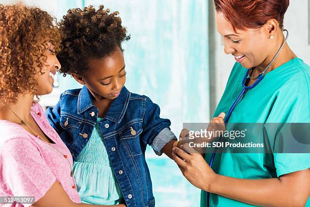 doctor applying bandaid to arm of little girl after vaccinations - african american band aids stock pictures, royalty-free photos & images