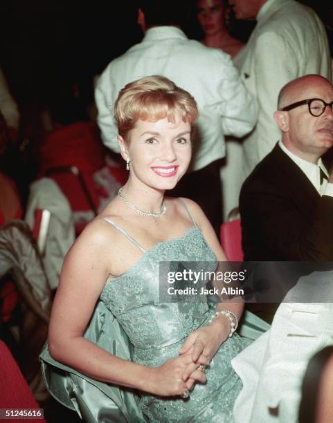 Circa 1955, American actor and singer Debbie Reynolds, wearing an evening dress, smiles while sitting in the crowd at a formal event, 1950s.