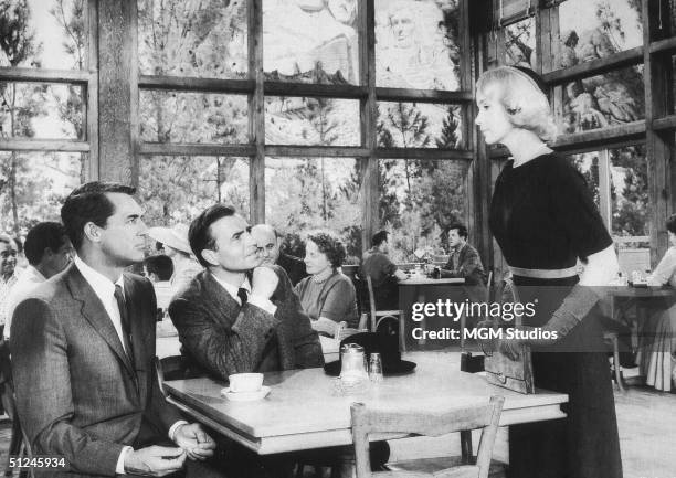 British actors Cary Grant and James Mason look up from their table toward American actor Eva Marie Saint, in the dining room below Mount Rushmore, in...