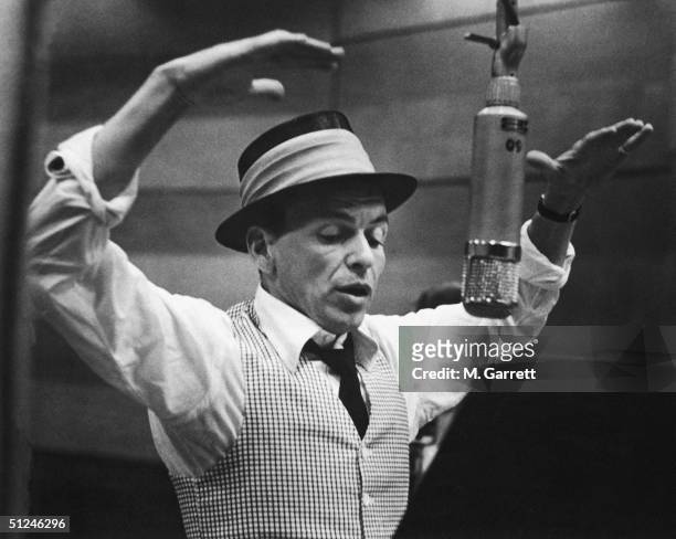 American singer and actor Frank Sinatra gestures with his hands while singing into a microphone during a recording session in a studio at Capitol...