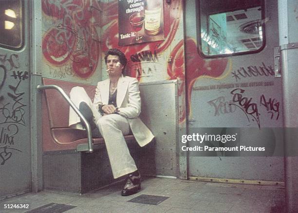 American actor John Travolta sits on a bench inside a subway car painted with graffiti in a still from director John Badham's film 'Saturday Night...