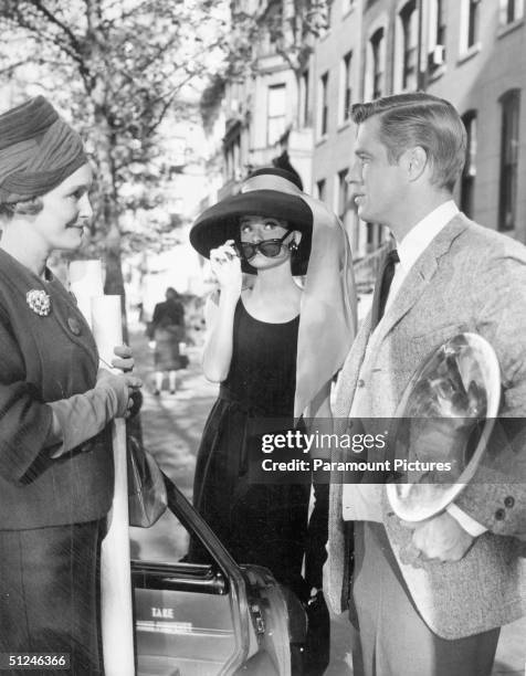 Patricia Neal converses with George Peppard as Audrey Hepburn peers over her sunglasses in a still from director Blake Edwards' film 'Breakfast at...