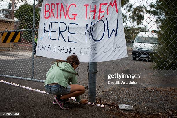 Young girl places a candle outside the gates of a refugee detention centre during a candlelight vigil as protestors stand in solidarity with refugees...