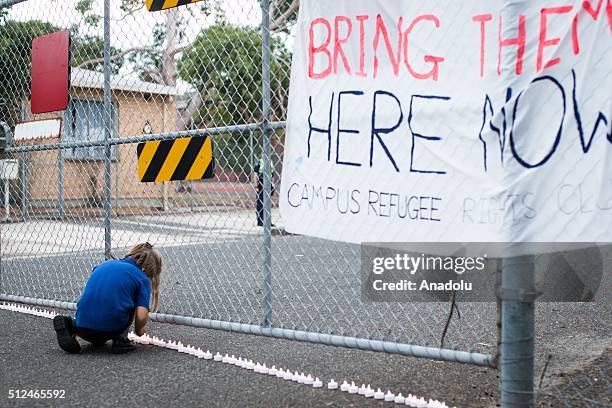 Young girl places a candle outside the gates of a refugee detention centre during a candlelight vigil as protestors stand in solidarity with refugees...